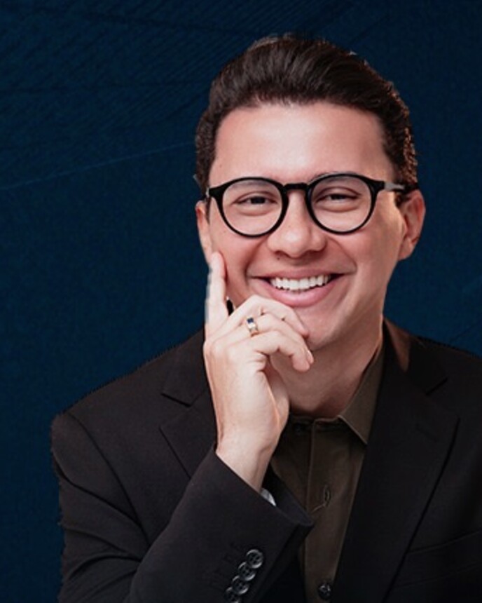 Natan Andrade de terno, sorrindo, retrato de estúdio sobre fundo escuro.